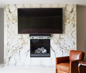 Television mounted above a fireplace with ceiling to floor white marble slab with black and gold veins