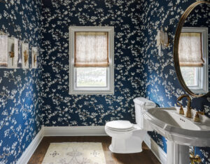 Powder room with white floral wallpaper with a navy background, white fixtures, and warm wood flooring and accents.